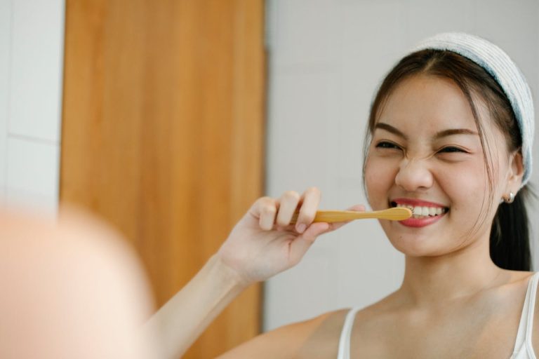 Seorang wanita sedang memberus gigi menggunakan berus gigi kayu, menunjukkan amalan penjagaan gigi untuk memastikan gigi putih dan sihat. Pemutihan gigi secara semula jadi boleh meningkatkan keyakinan diri.